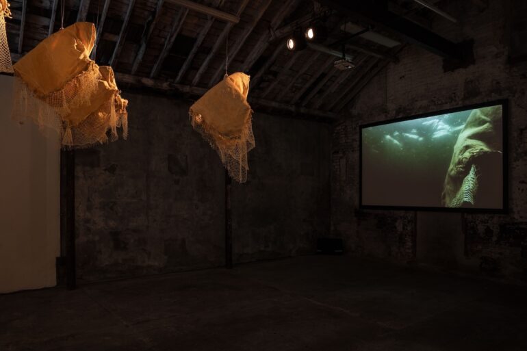 Bettina Seitz, exhibition view Underwave, The Complex, Dublin, 2024, 5 suspended sculptures and 7 floor based sculptures in Carnauba wax, cotton blankets, fishing net and buoys and single screen HD digital film projection of the sculptures filmed underwater in Sligo Inner Bay, total duration of 4 short films 5 min 36 sec, exhibition produced by the Centre for Creative Practices, ‘Underwave’ films originally commissioned by Tread Softly in 2020, supported by the Arts Council and Creative Ireland, photo by Kate-Bowe O’Brien.