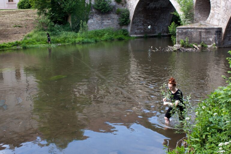 Sophie Foster (2018) CO-ORDINATION. Public intervention and Performance A collaborative performance with Maedeh Nassouri at the Ilm park in Weimar. Responding to "bridging" as a concept, we worked together to keep the connection using a piece of string as we walked along the river. Photographer: Vincent Brière.